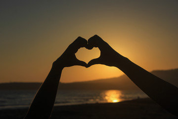 silhouette of two hands forming a heart during sunset