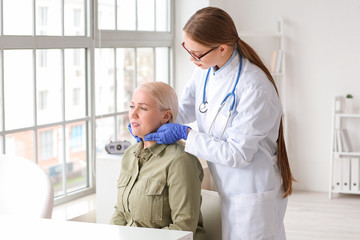 Doctor examining senior woman with thyroid gland problem in clinic