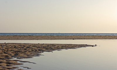 landscape of a sandy beach with two strips of water, one blue and choppy and the other calm