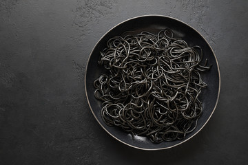 Black pasta spaghetti squid Ink in black bowl on black. Top view. Space for text.