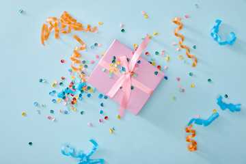 top view of colorful confetti near pink gift box on blue background