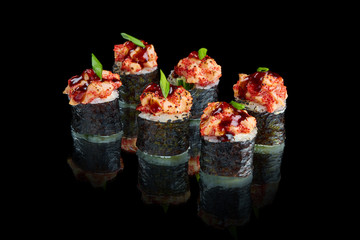 Spicy sushi roll with seared salmon, onions, tobiko caviar and unagi sauce on a black background with reflection. Japanese cuisine