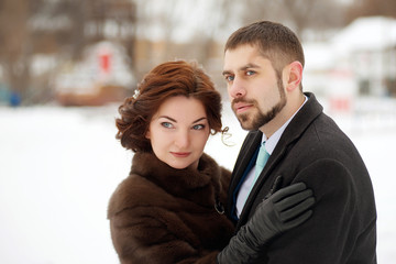 Loving couple hugs and looks away in the winter park. Winter wedding.