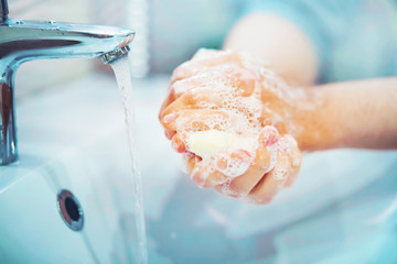 A man carefully washes his hands with soap and thick foam in the bathroom over the sink, from the...