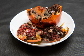Spoiled rotten sliced pomegranate with mold on a white plate, closeup