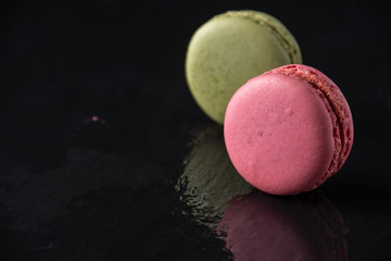 Close-up of pink and green macaron, with selective focus, on wet slate stone, with reflection, horizontal