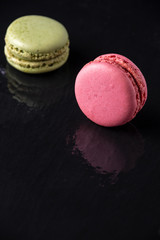 Top view of pink and green macaron, with selective focus, on wet black slate stone, with reflection, vertical