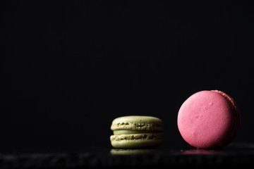 Close-up of pink and green macaron, with selective focus, on wet black slate stone and black background, horizontal