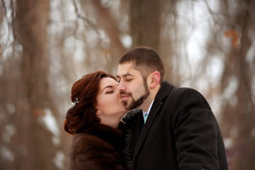 Close-up of a beautiful brown-haired woman kisses her man on the cheek in a winter park.