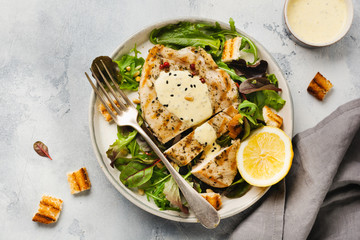 Homemade grilled turkey steak with sauce, broccoli, arugula and chard in a ceramic plate on a light concrete background. Top view.