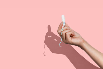 Woman's hand holding a clean cotton tampon on the pink background. Direct light. - obrazy, fototapety, plakaty