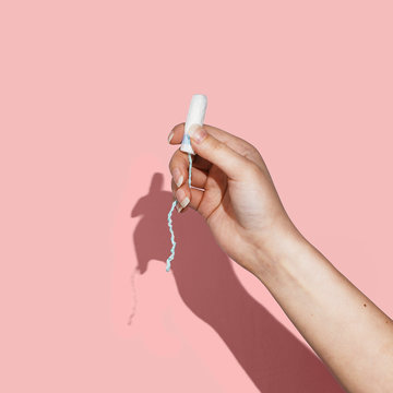 Woman's hand holding a clean cotton tampon on the pink background. Direct light. Square image.