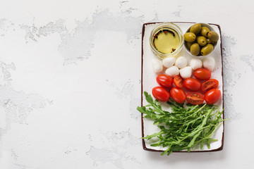 Mozzarella, cherry tomatoes and arugula served in white ceramic rectangular plates with olive oil over grey texture background. Flat lay