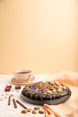 Homemade chocolate brownie cake with caramel cream and almonds with cup of coffee on a white and orange background. Side view, selective focus, copy space.