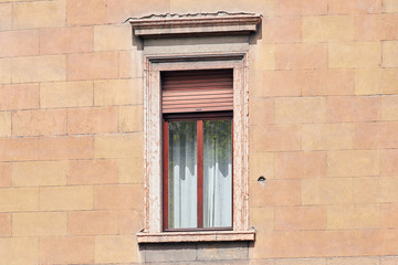 Italian window on the sandy-yellow bricked wall facade with open brown color roller shutters