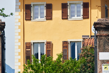 Fototapeta na wymiar Italian windows on the yellow wall facade with open brown color classic shutters