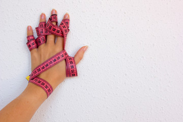 hand of a white woman close up on the left side of the picture with a pink centimeter wound around her hand on the white background