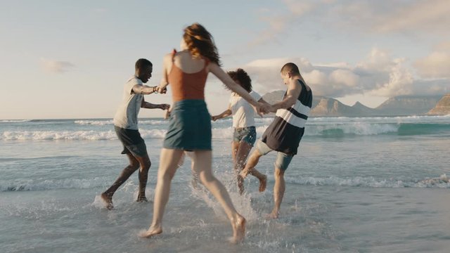 Multiracial friends playing childhood games on the beach. Group of men and woman playing ring around the rosy at the sea shore.
