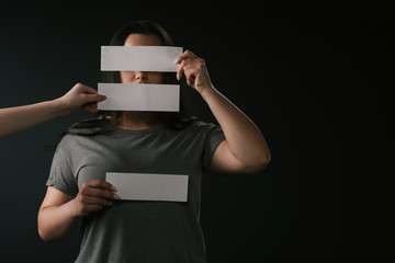 Front view of plus size girl covering face under empty cards with copy space on black background