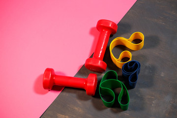 Red dumbbells and elastic bands for sports on a pink background. Healthy lifestyle. Fitness...