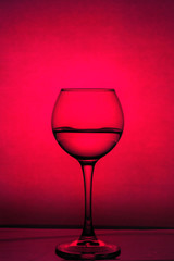 Wine glass with liquid on a red background. Backgrounds and textures.