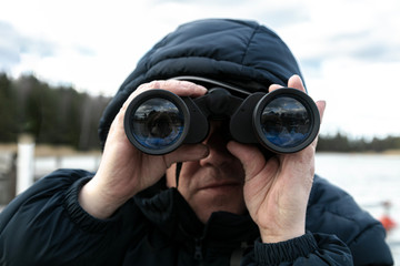 A man on the riverbank is looking through binoculars