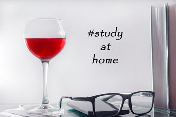 The concept of online education, home study. On the table is a glass of red wine, a row of books, glasses, a smartphone and a workbook.