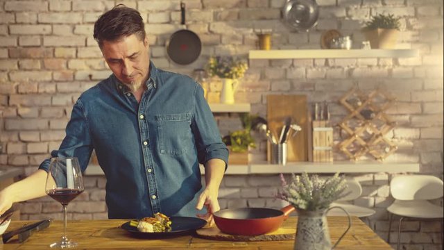 White casual man cooking in kitchen at home serving food to plate on dinner table