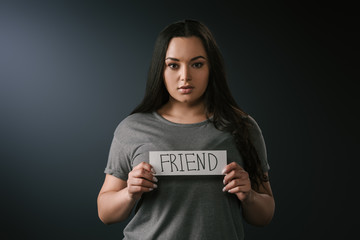 Front view of beautiful plus size girl holding card with word friend on black background