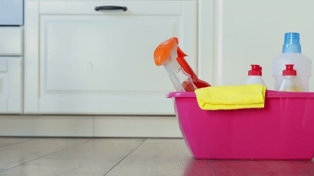 Various bottles of cleaning products and detergents, washcloths in a pink bucket in the room on the floor