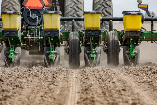 Closeup of tractor and planter in farm field planting corn or soybeans seed in dry, dusty soil during spring season