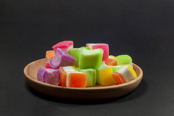 Multi colored jelly in a wooden tray against a black patterned background