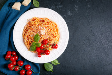Spaghetti with tomato sauce and cherry tomatoes with basil on a dark background