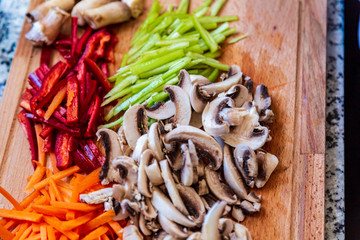 Chopped vegetables arranged on cutting board on wooden table, top view.
Mushrooms, red and green peppers, carrots
