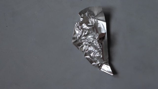 chocolate bar is unpacked, divided into slices and eaten. Foil packaging crumples and disappears from the grey textural background. Stop motion animation concept.
