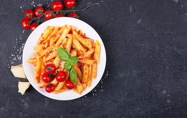 Pasta penne with tomato sauce, fresh basil, roasted tomatoes and parmesan on the dark background