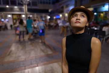Young beautiful Asian tourist woman thinking and sitting outdoors at night