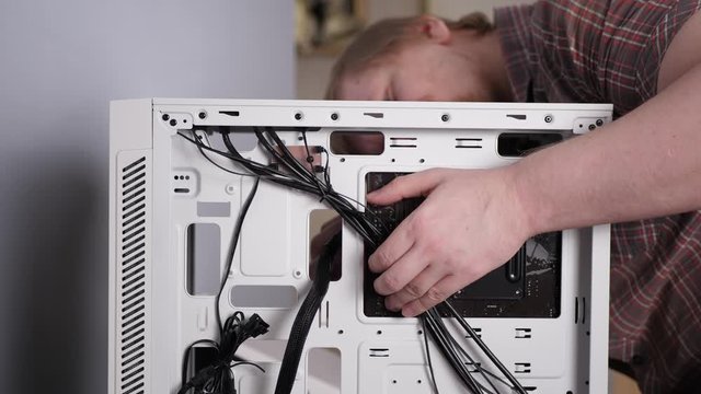 Faceless caucasian technician connects black electrified cables to motherboard in white system unit, muscular man builds personal desktop computer.