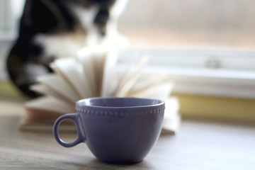 Cup of coffee or tea, open book and a cat at home. Selective focus.