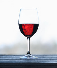 Glass with red wine on a wooden surface against a light blurred background