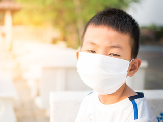A sadness Asian boy wears a white T-shirt and wearing a face mask in a sunrise natural blurred background.