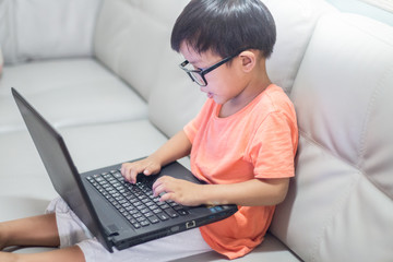 little boy Wear glass use laptop on sofa in home, work from home