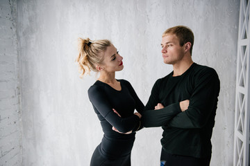 The guy and the girl in tracksuit. Black sports uniform. Male and female athletes. Pumped up body. Triathlon. Morning work-out. Set of exercises for body. Classes in pair. Workout together at home.