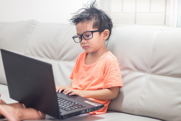 Fototapeta na wymiar little boy Wear glass use laptop on sofa in home, work from home