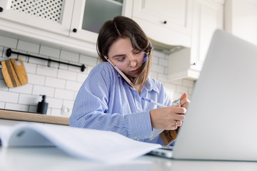 Obraz na płótnie Canvas Young woman in scandinavian style kitchen interior and working on a laptop. Home quarantine during Covid-19 pandemic Coronavirus. Distance work from home concept. Female freelancer working at home