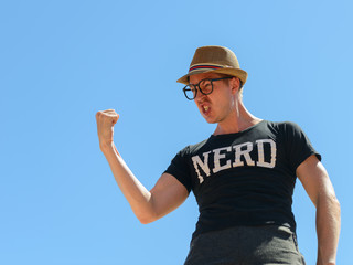 Young nerd tourist man with fist raised against blue sky
