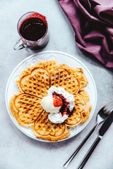 Heart-shaped freshly baked waffles with vanilla ice cream and red berry sauce