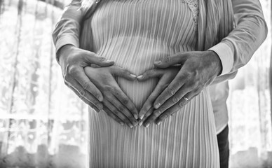 Pregnant women wrap her arms around the belly in the form of the heart. Family concept.