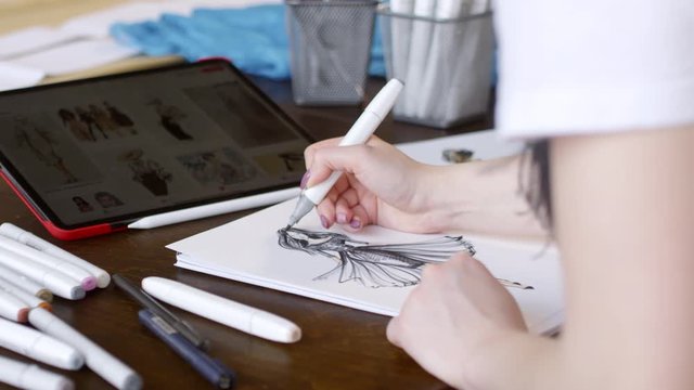 Close up shot of hands of female fashion designer drawing beautiful dress from picture on digital tablet