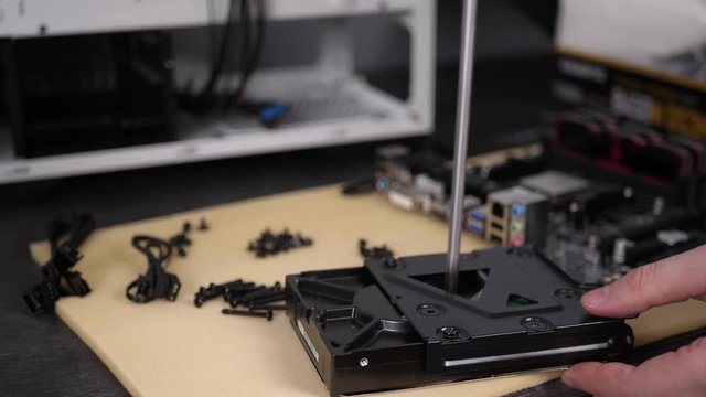Closeup male hands with a screwdriver twirl screw into a metal panel and a hard drive for installation in the system unit, the technician assembles a personal computer in parts into a case.